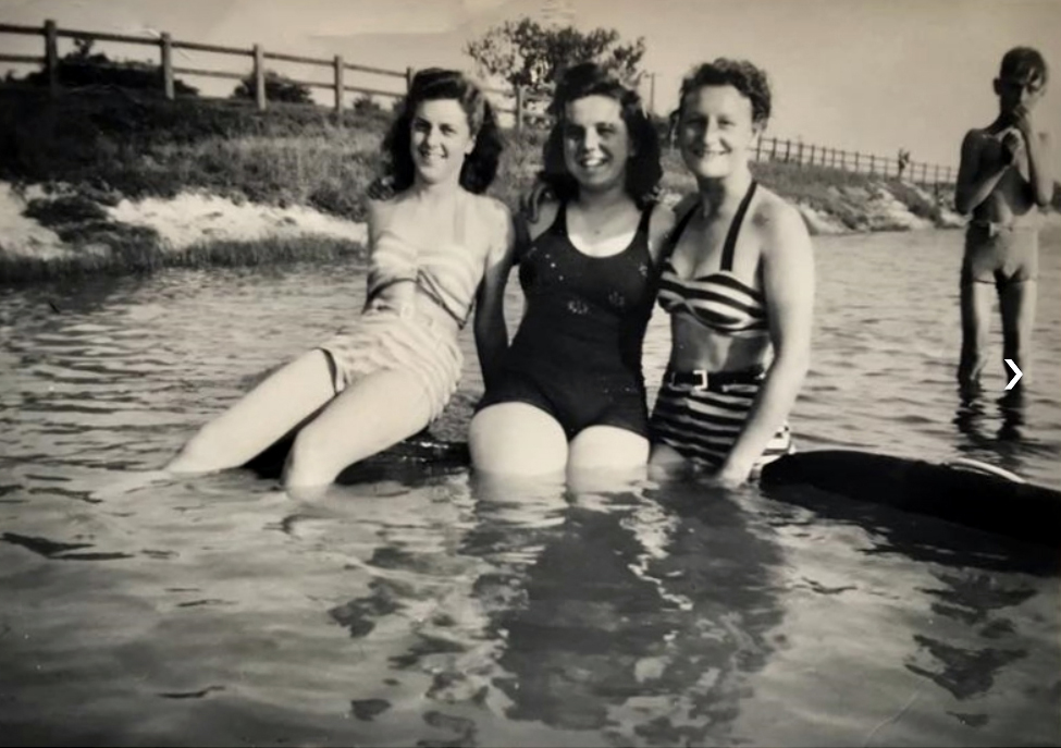 three women in swimming costumes in water, smiling