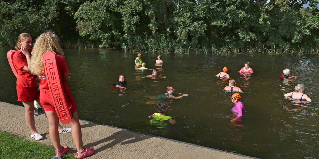 swimmers in a river with two lifeguards on a jetty