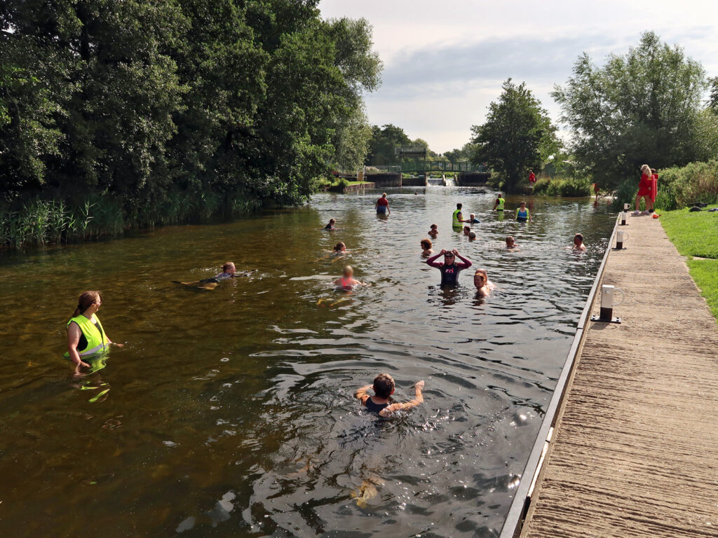 swimmers and volunteers in river with lifeguard on jetty and distant view of staunch