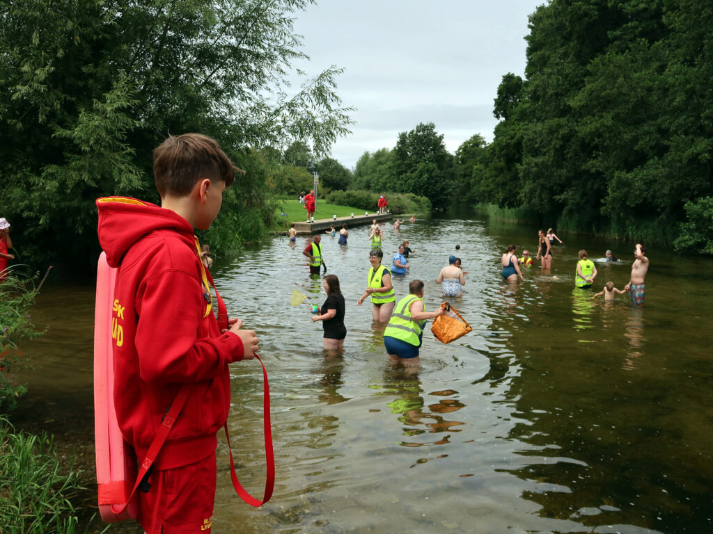 families and volunteers in river with lifeguards and volunteers, view of jetty