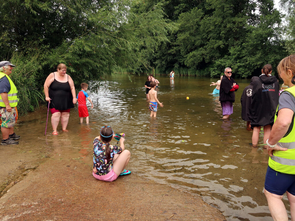 families and children playing in river at shallow edge with volunteers
