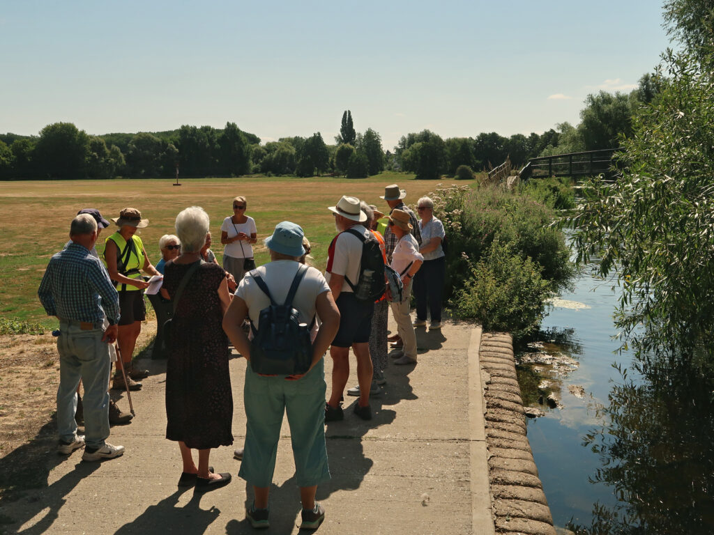 walkers listening to a talk at Jubilee Fields, river and bridge and fields beyond